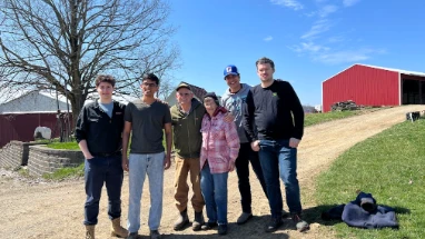 Six members of the Luzardo team standing together on a farm track, with a red barn and open pasture behind them